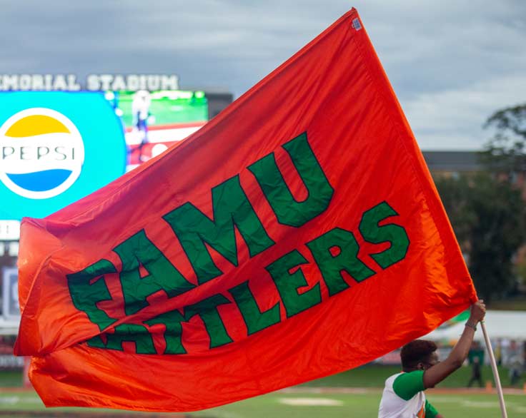 man with giant famu flag running on football field