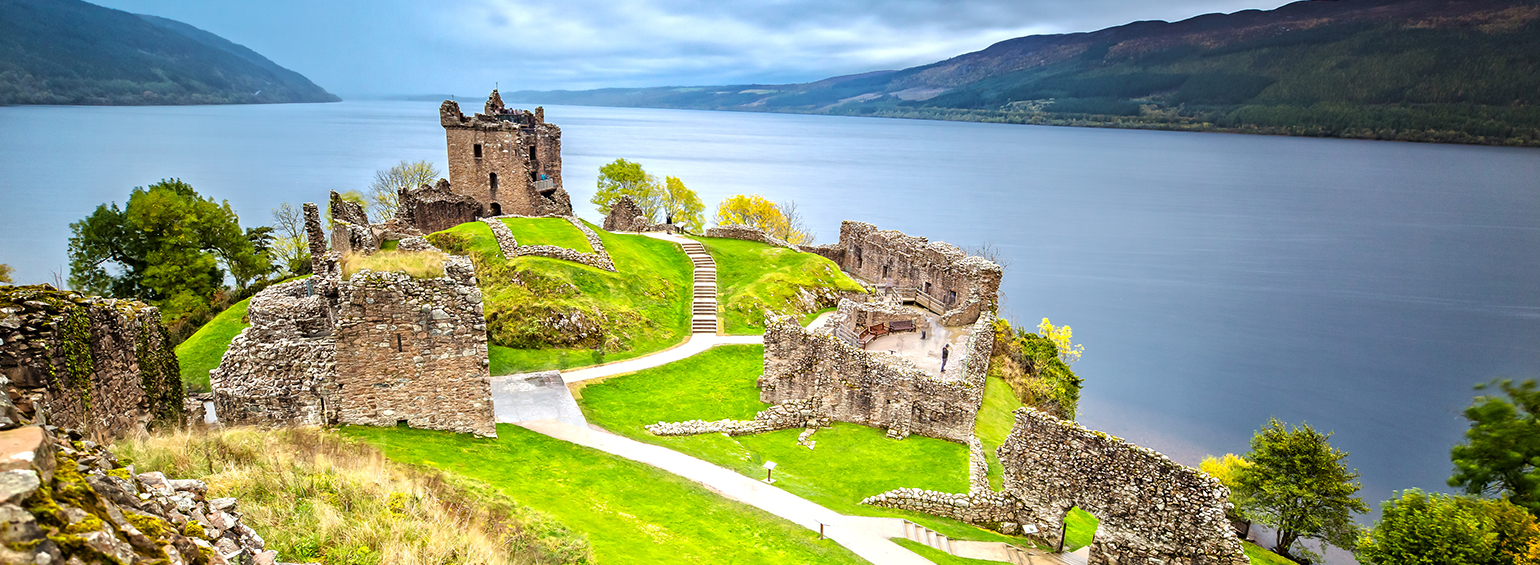 castle in ruins overlooking body of water with mountains in the background