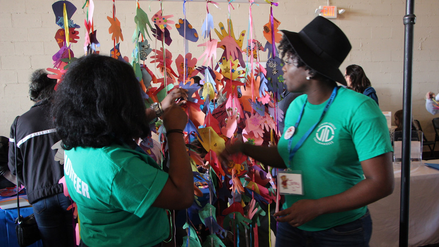 two women in green volunteer shirts next to strung up paper hands