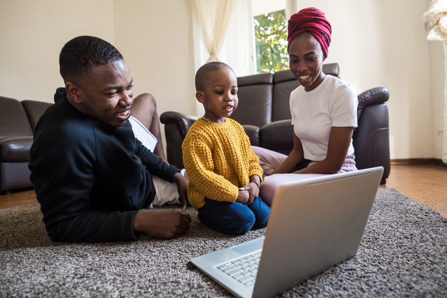 family on floor with toddler watching something on the laptop